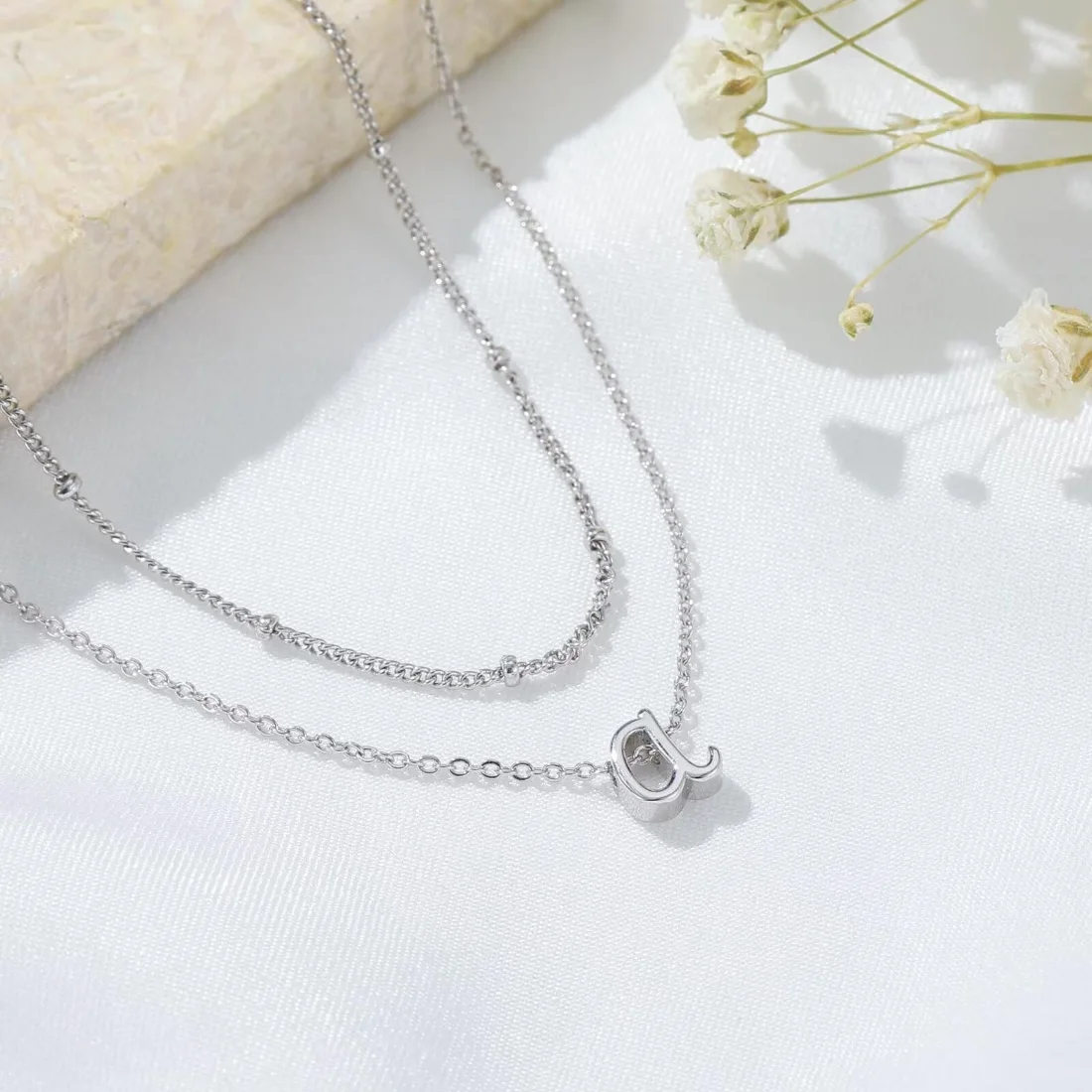 A silver tone initial necklace laid on a light surface